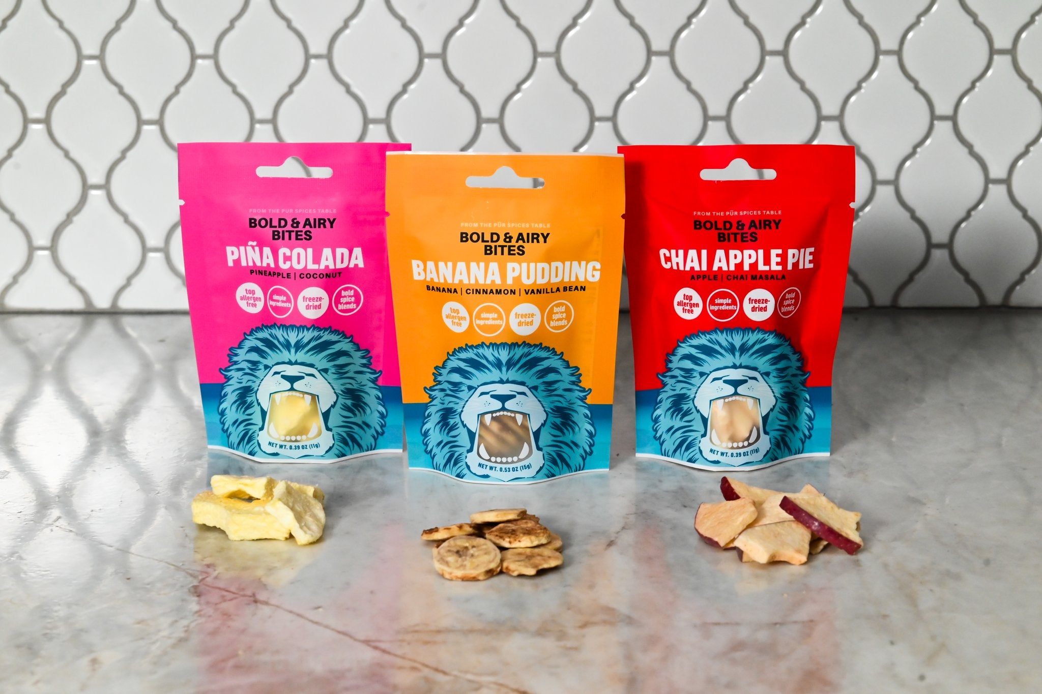 Three colorful packages of Bold &airy snacks on a marble surface with a tiled wall background.